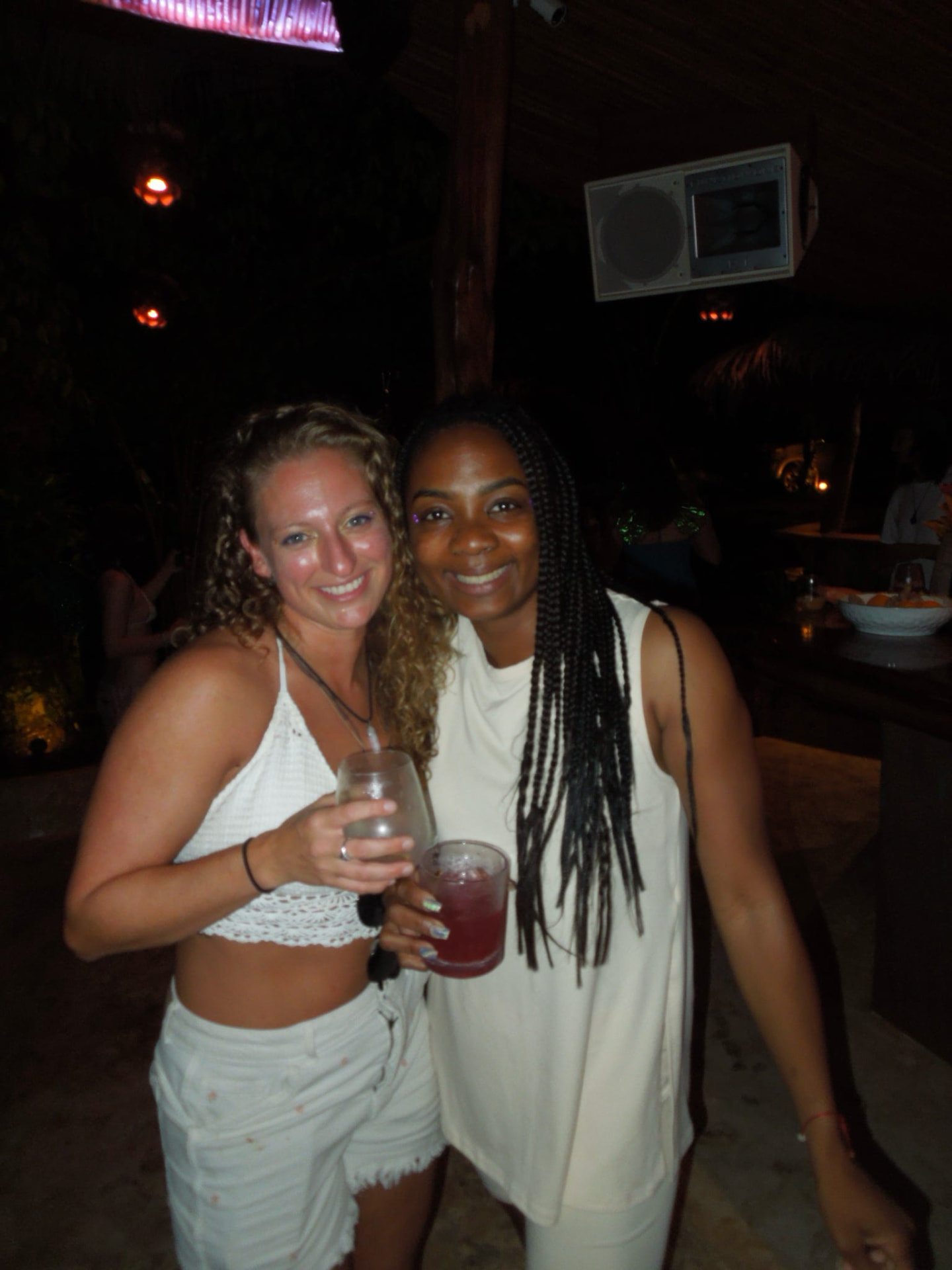 Two friends toasting drinks together at the bar in all white