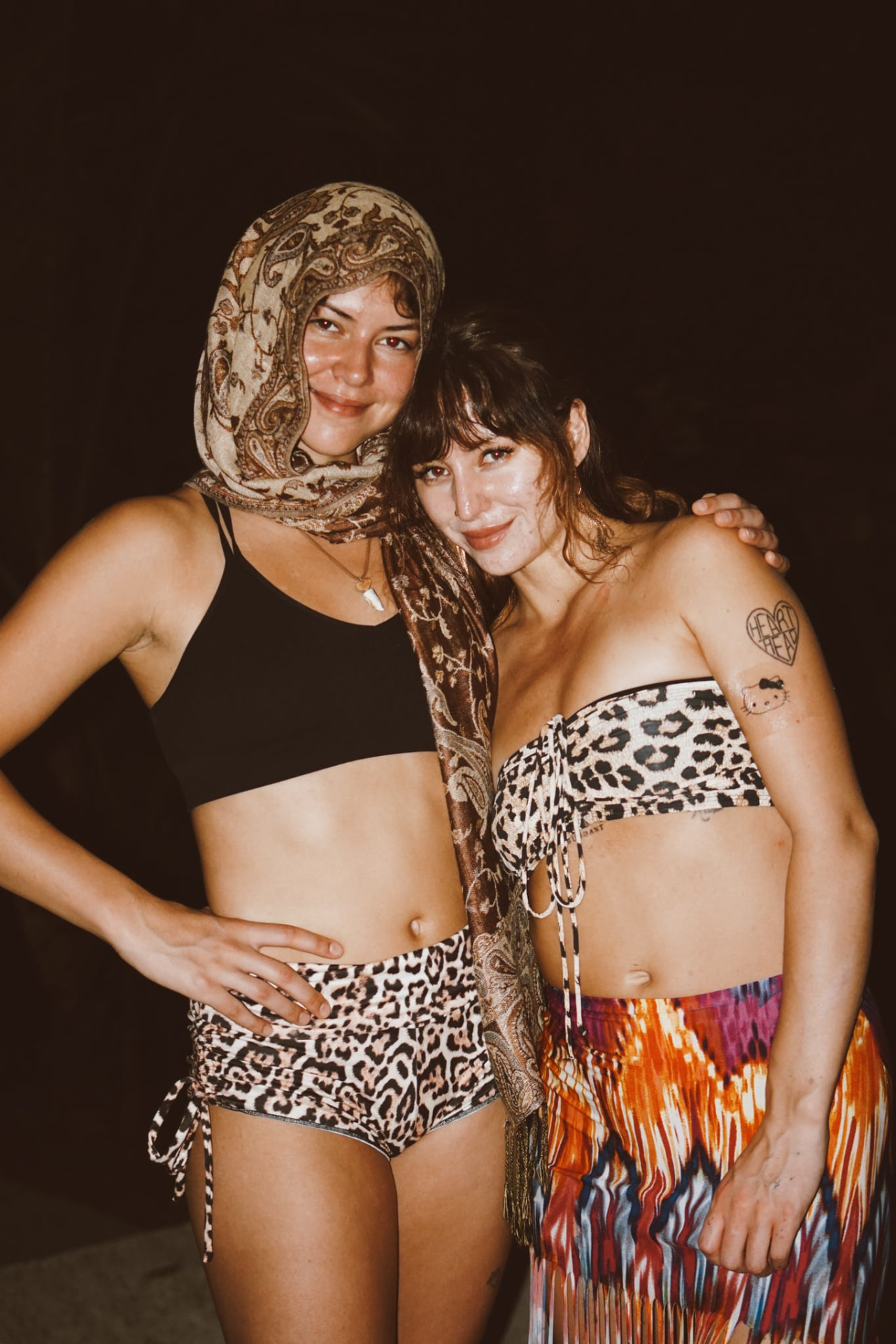 Two guests posing together in festival looks at night