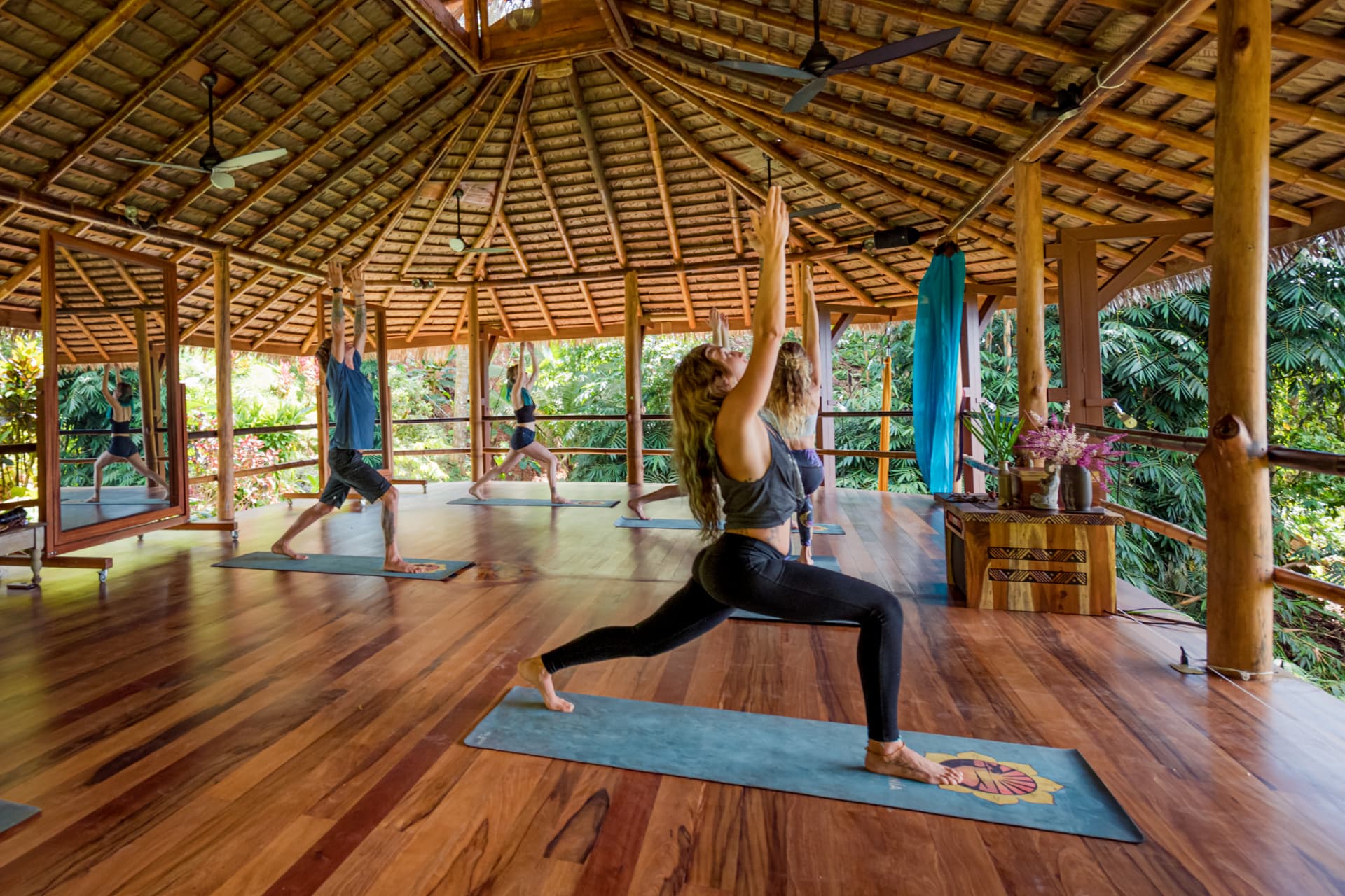 Group flowing through warrior pose in the open-air yoga shala surrounded by jungle
