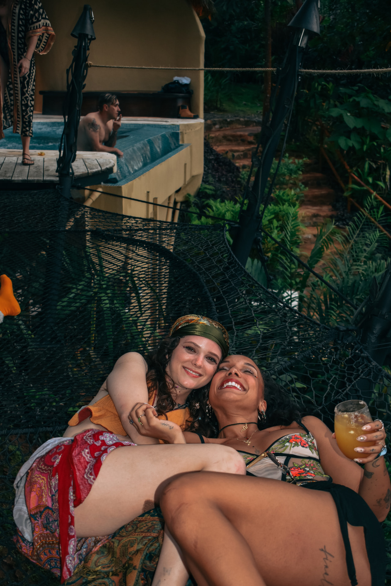 Two friends laughing together on the hammock nets with drinks