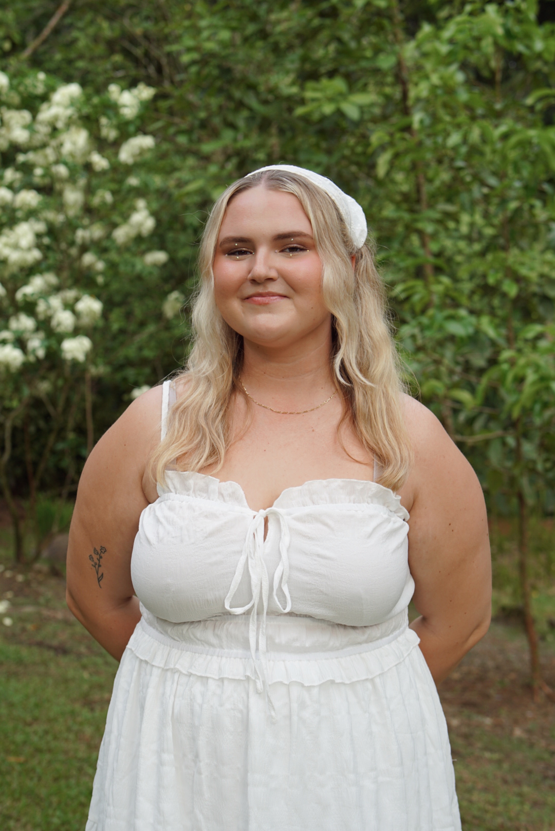 A guest in a white dress smiling in front of flowering jungle greenery