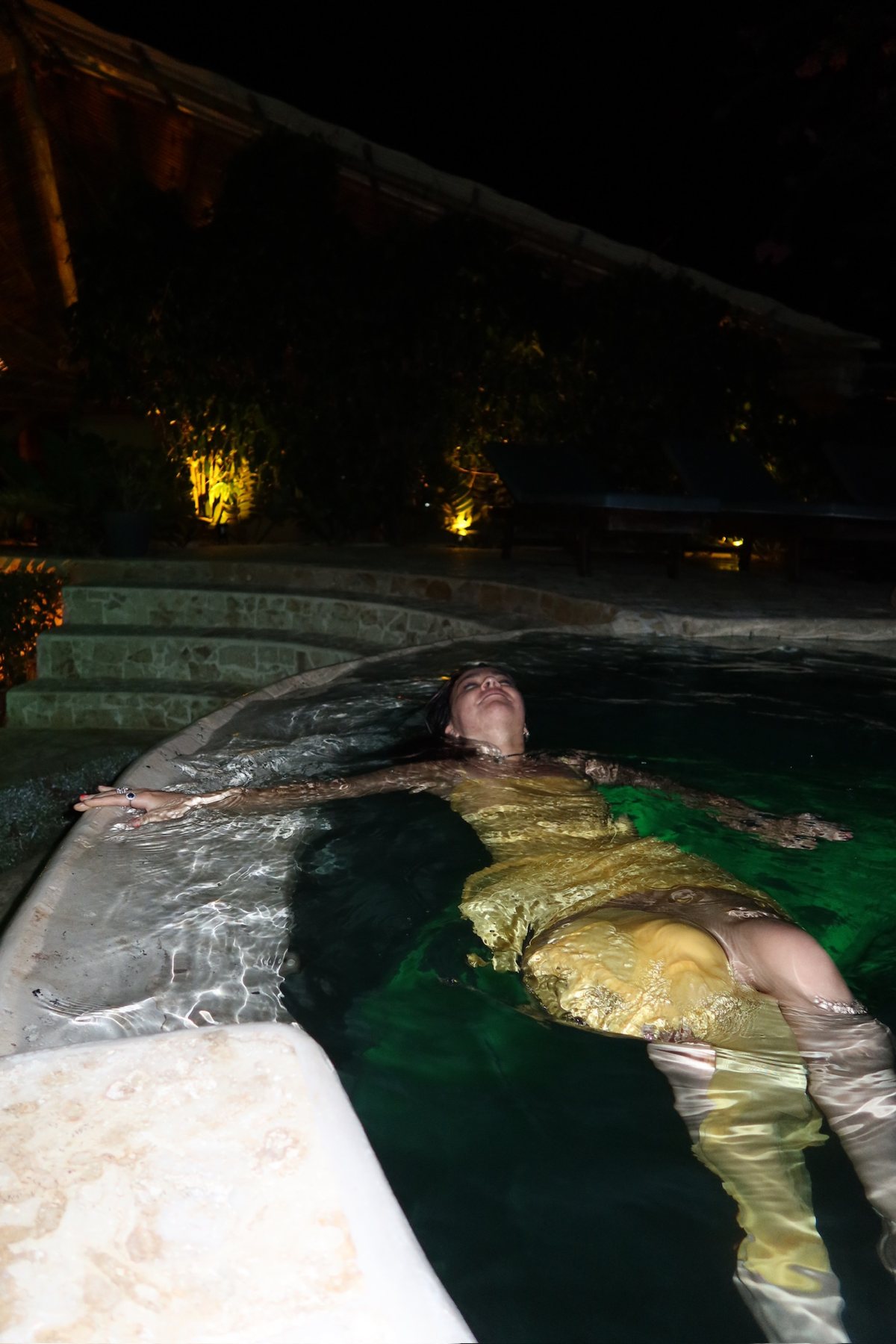Floating in the glowing pool at night in a silk dress