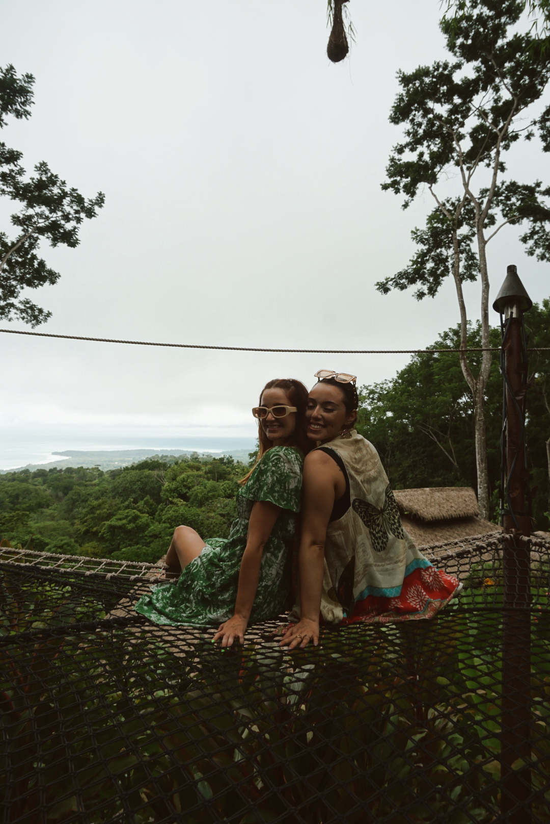 Two friends sitting together on the canopy net overlooking the Pacific