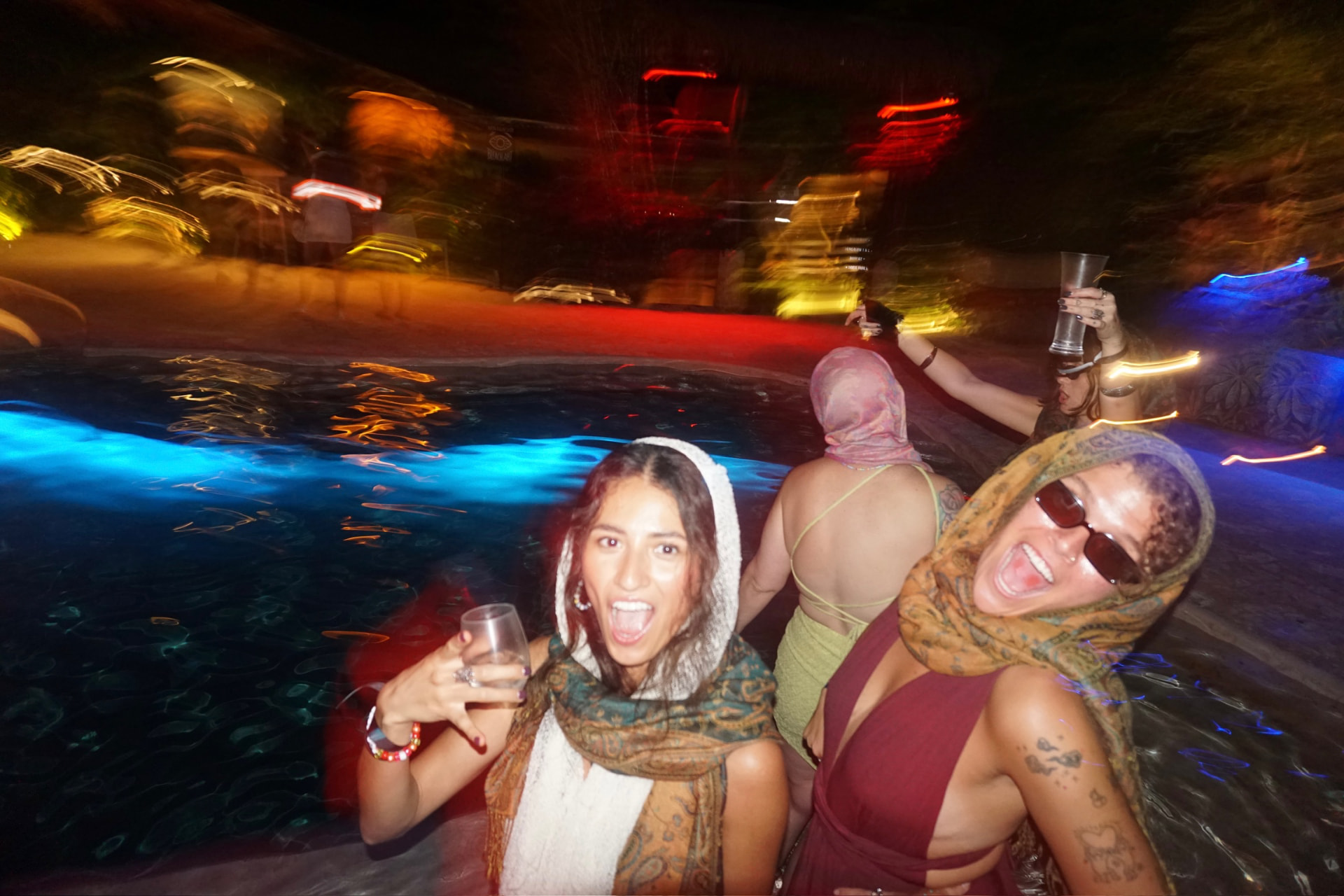 Late night in the lit-up pool, drinks up, everyone screaming