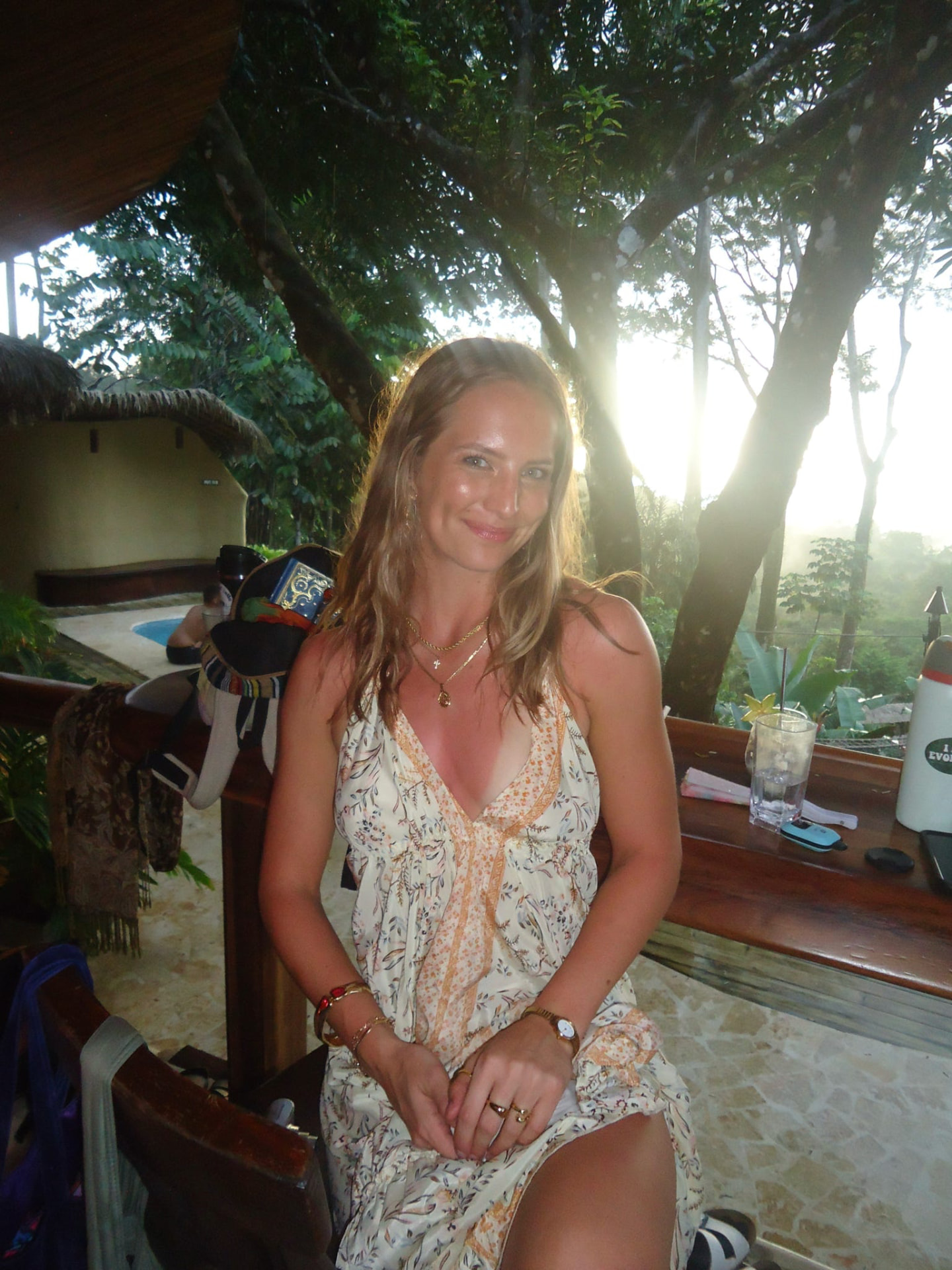 Guest in a flowing dress at the palapa bar as the sun sets through the trees