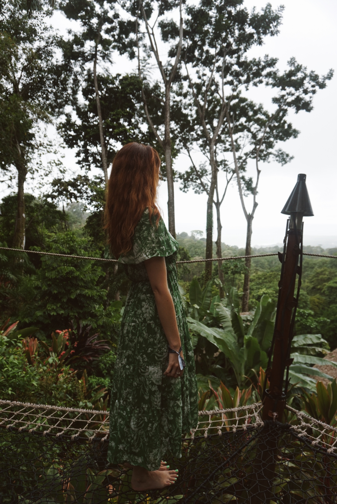 A guest in a green floral dress looking out over the jungle and ocean from the net deck