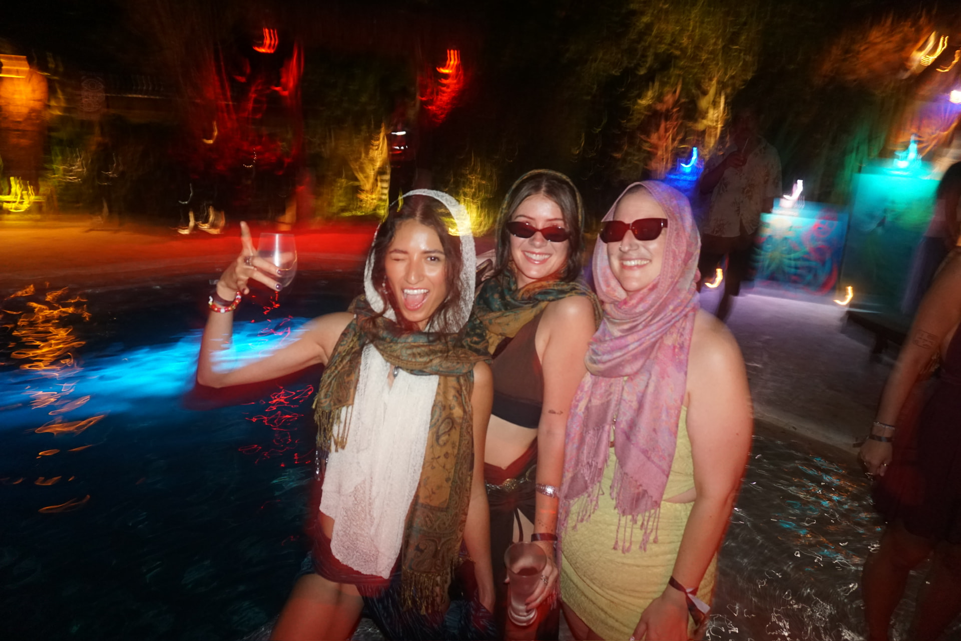 Three friends in scarves cheersing beside the glowing blue pool