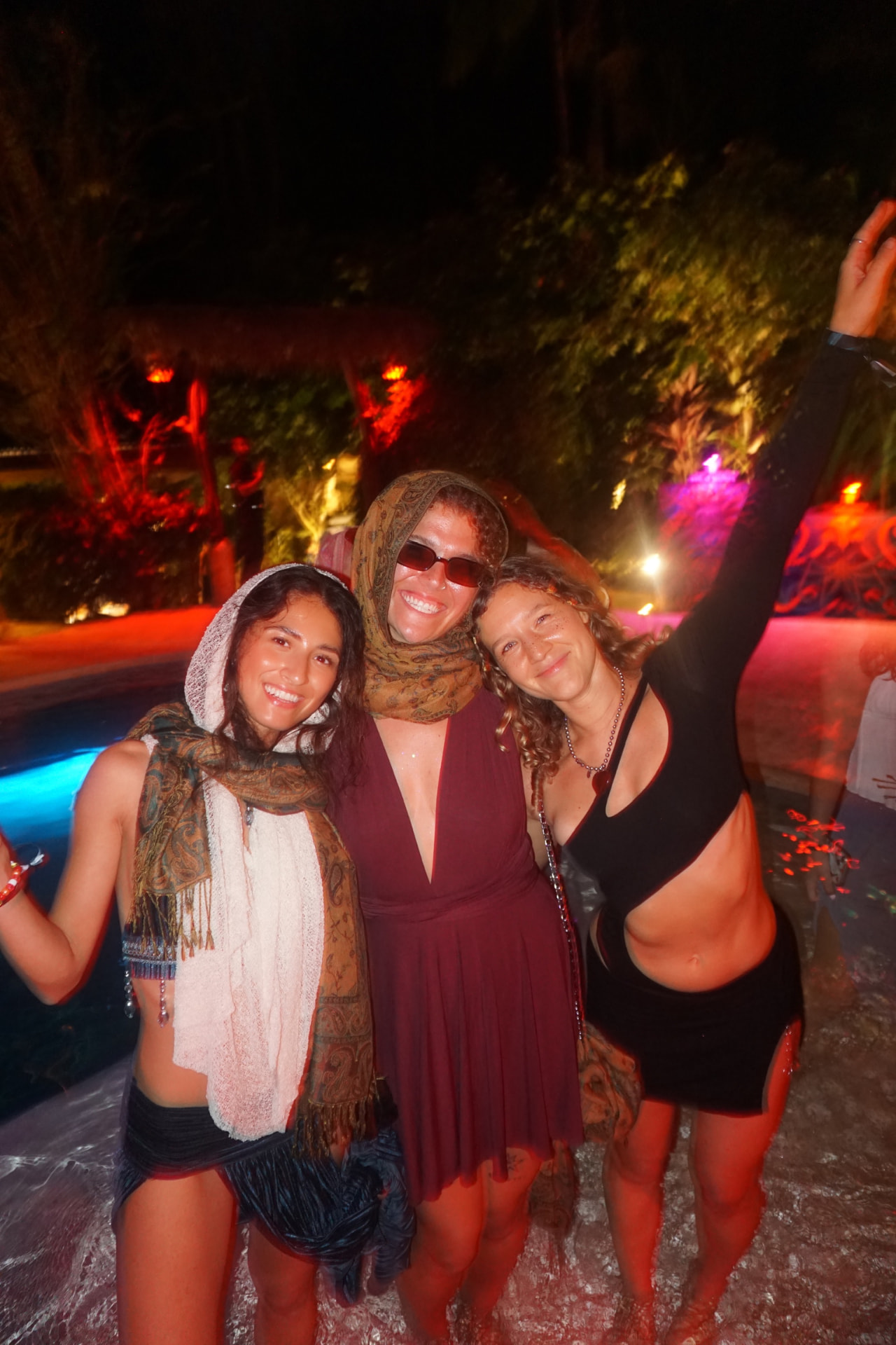 Three friends standing in the pool at night in silk scarves