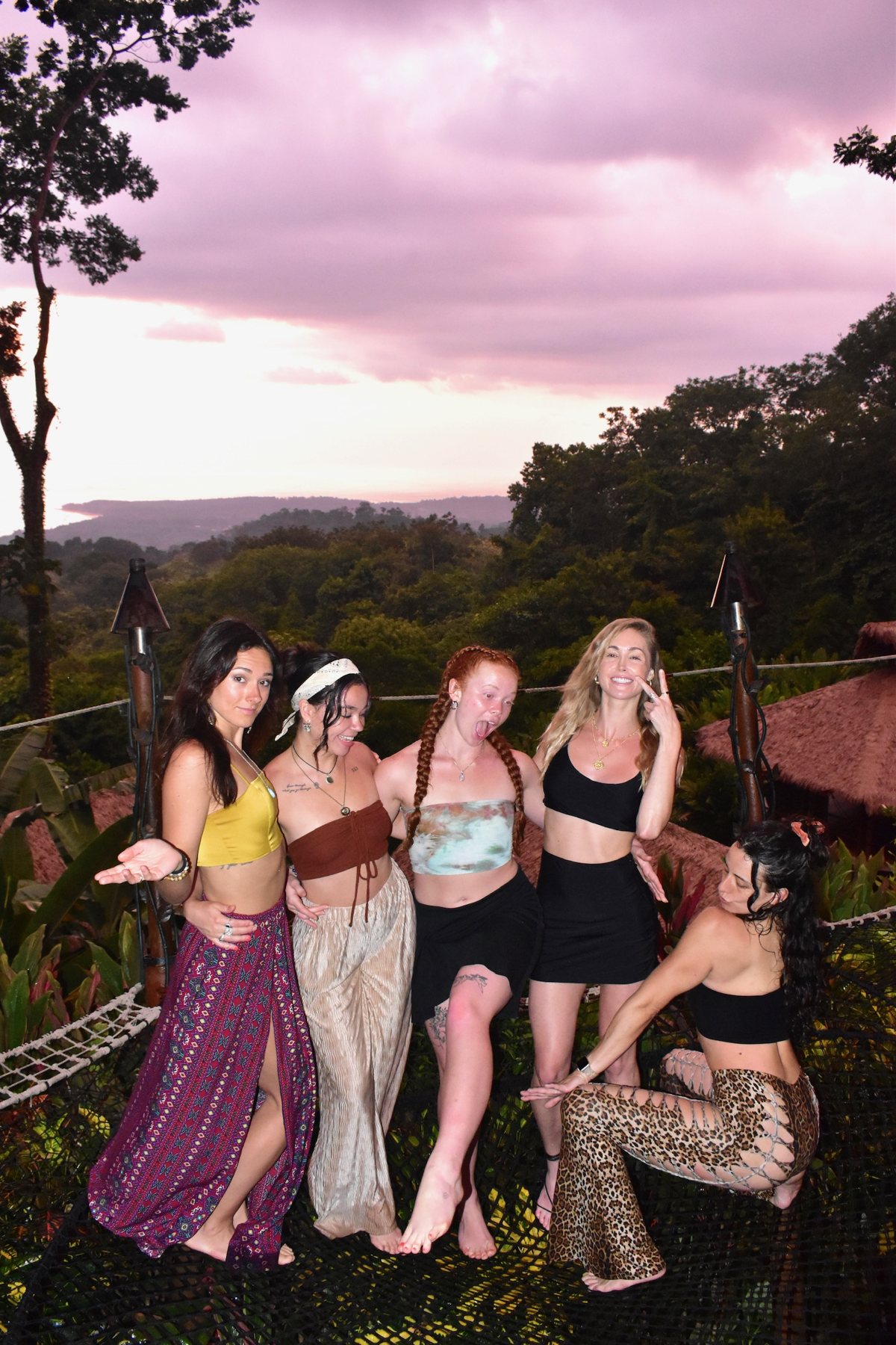 Five friends standing on the hammock nets under a pink sunset sky