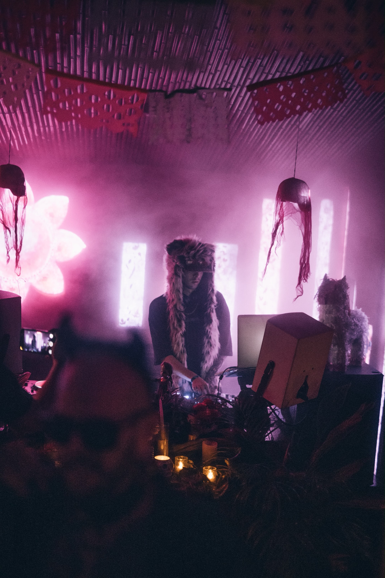 DJ in a furry hat playing under pink light and haze in the shala