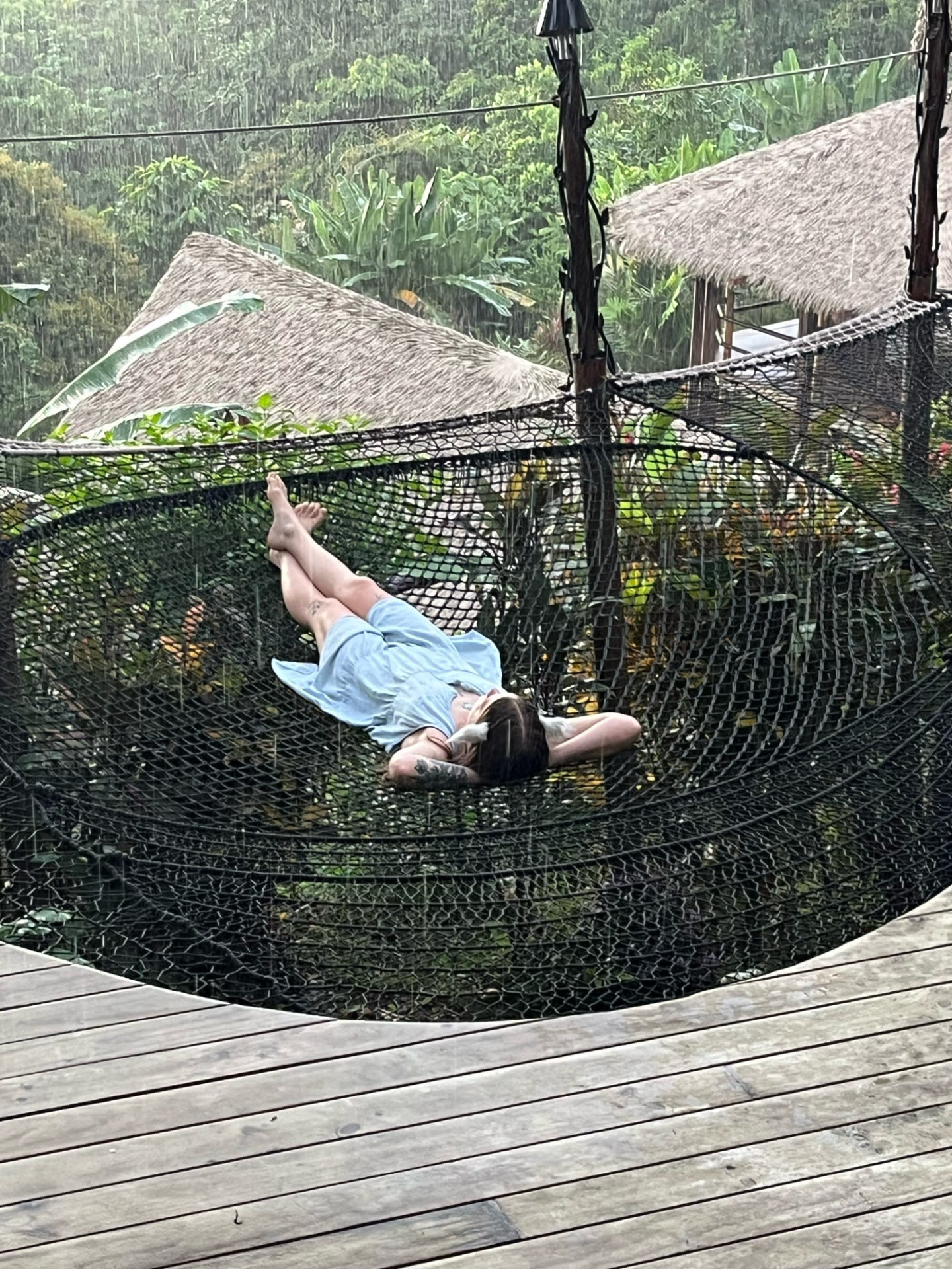 Guest resting in the hanging net while rain falls over the jungle