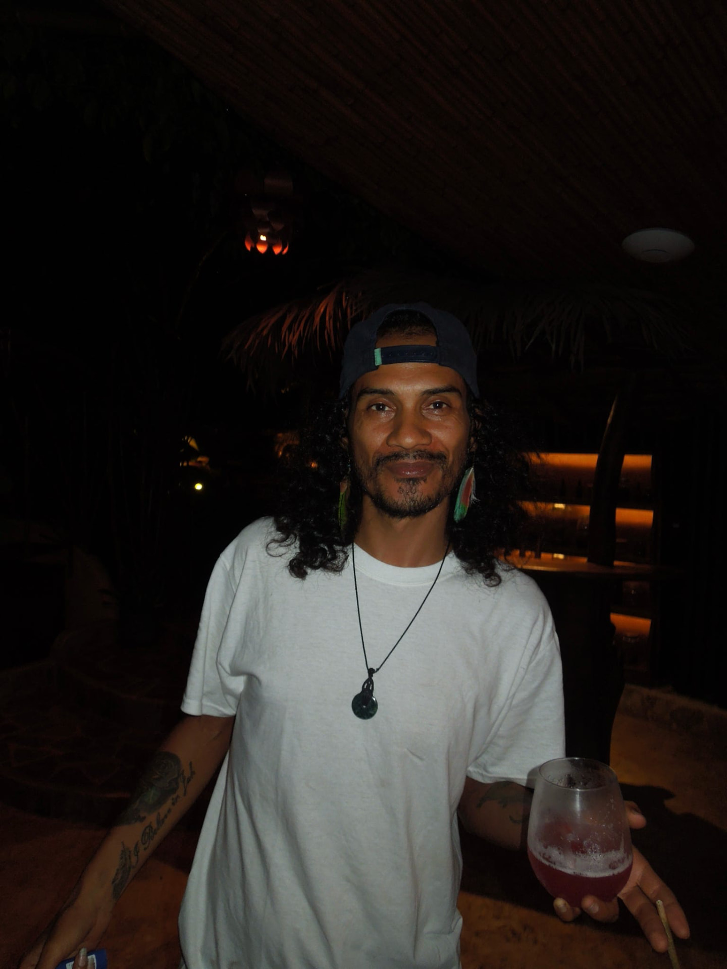 A guest smiling with a drink under the palapa at night