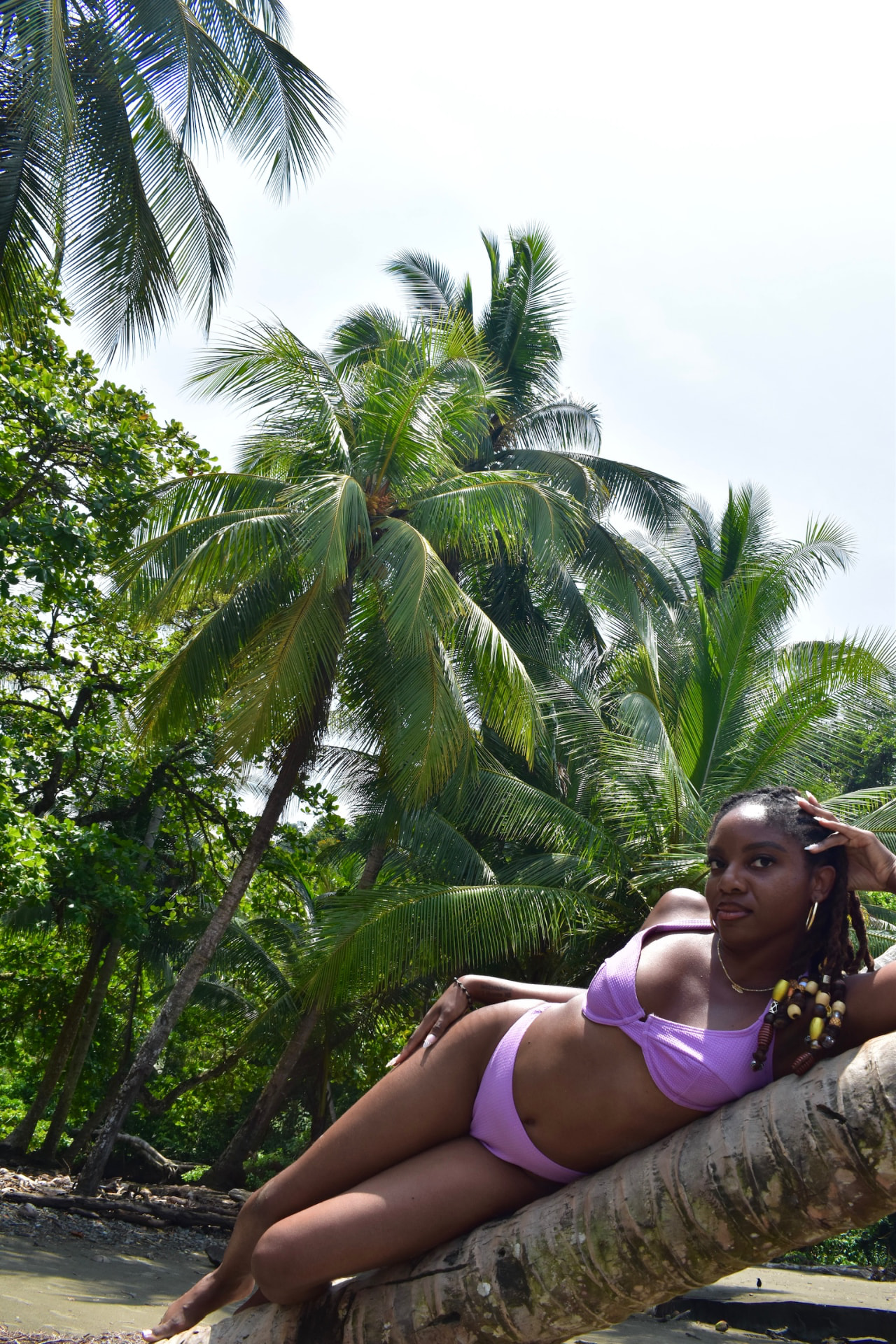 Guest lounging on a leaning palm trunk under the coconut palms