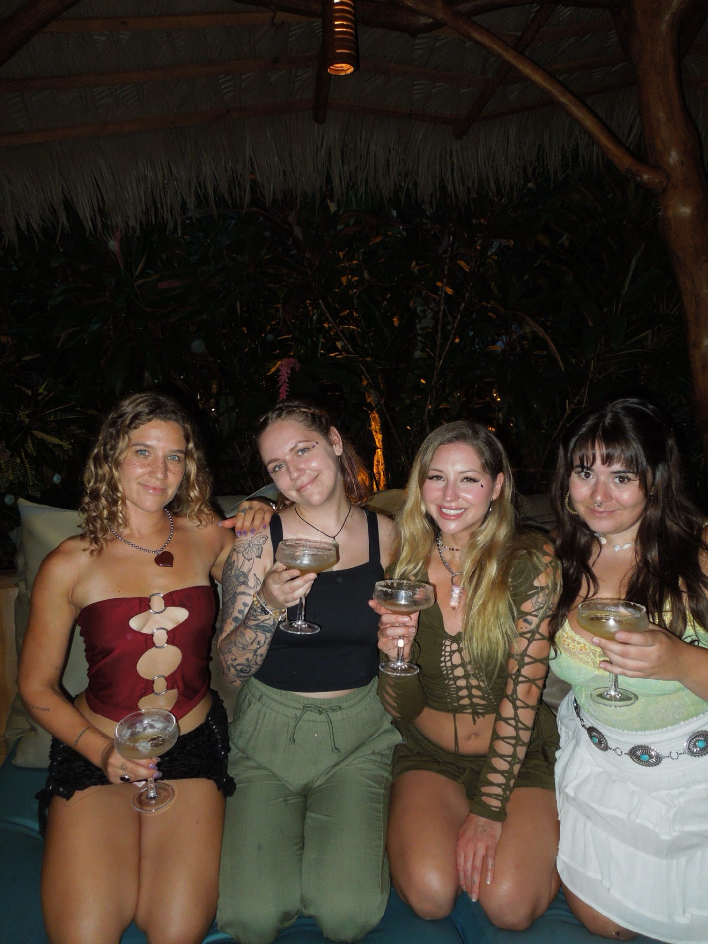 Four friends toasting with cocktails under the palapa at night