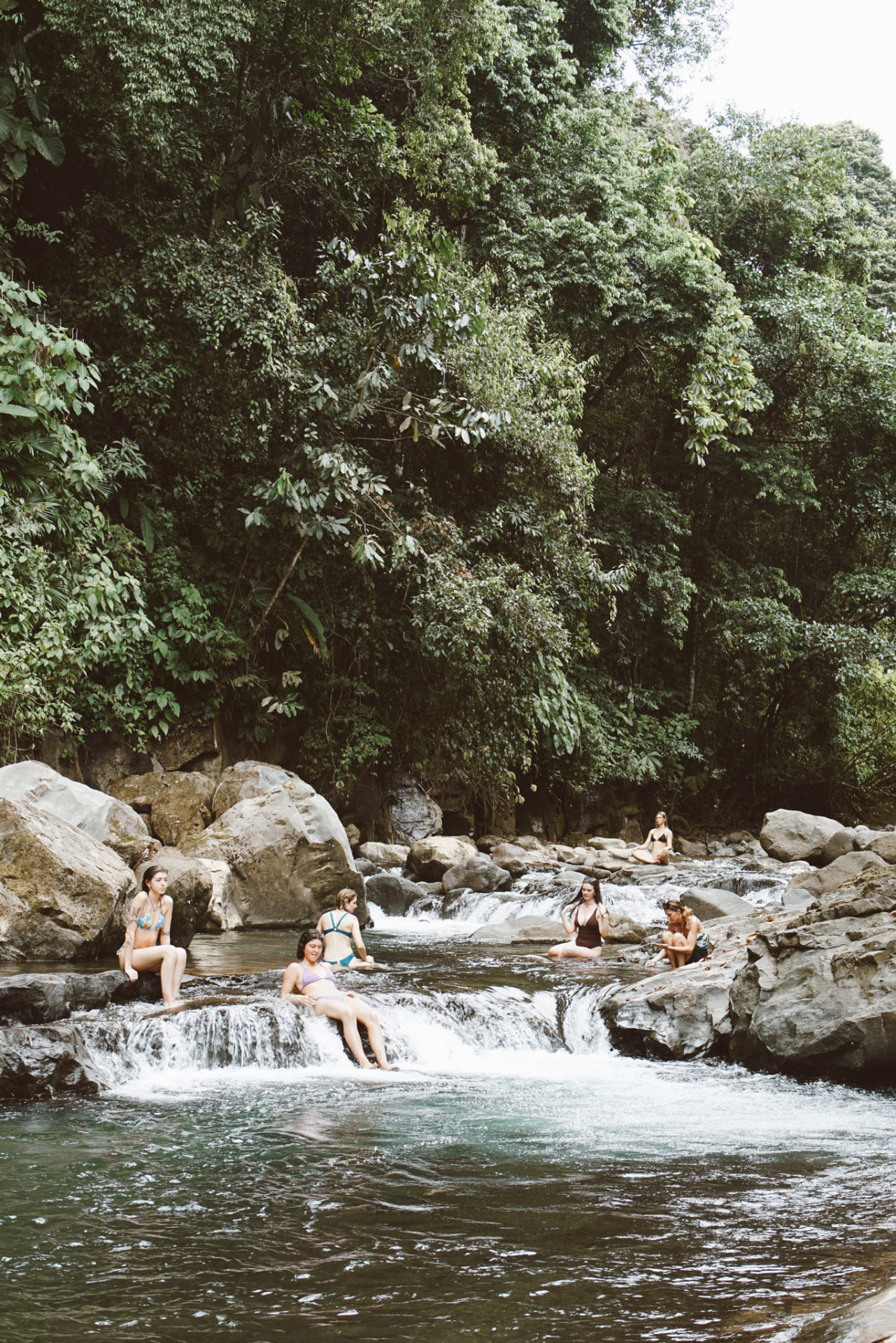 Guests lounging on the rocks of a jungle river cascade