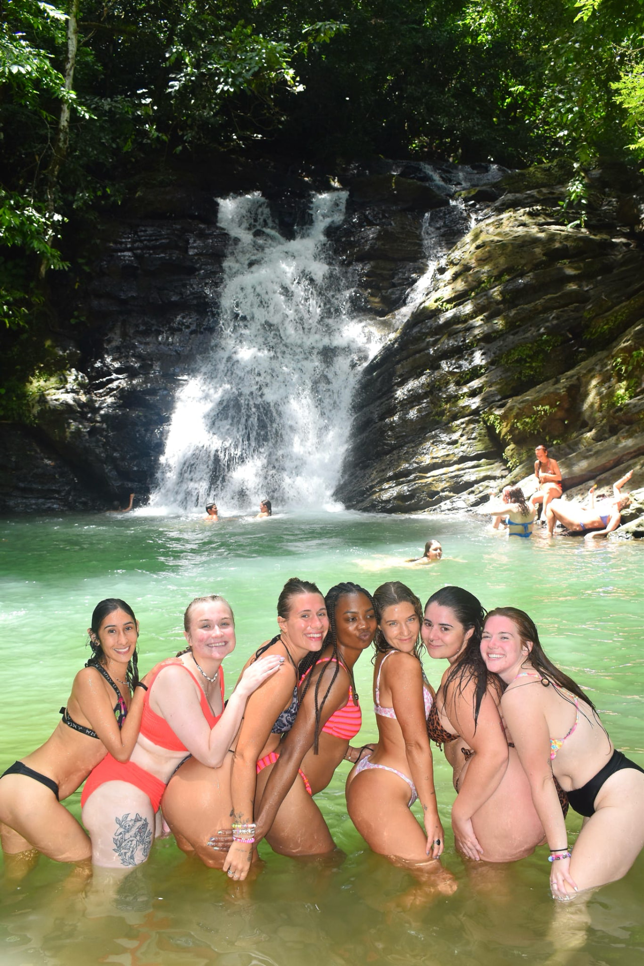 Seven friends posing together in a turquoise waterfall pool