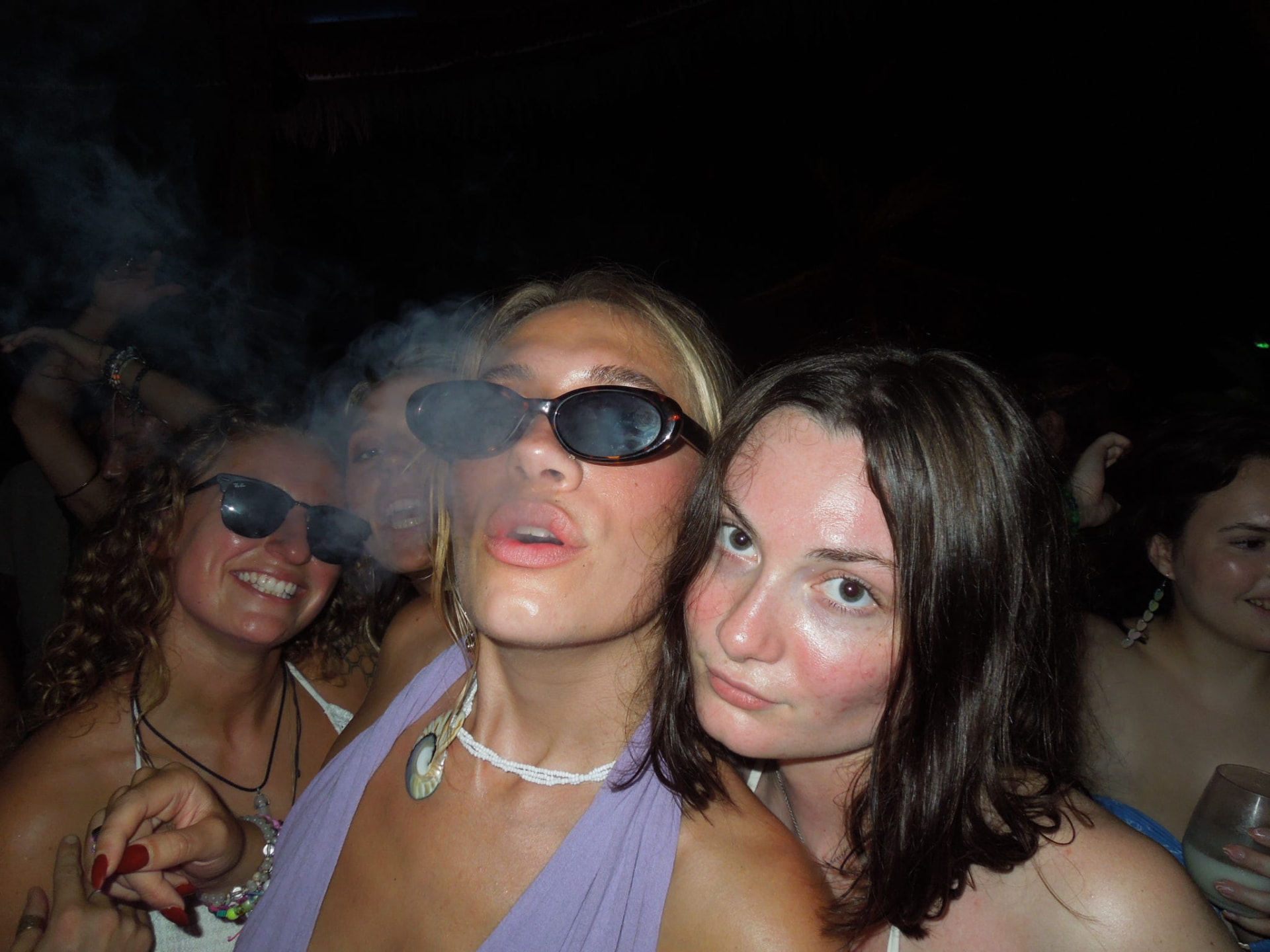 Friends in sunglasses posing together on the smoky dance floor
