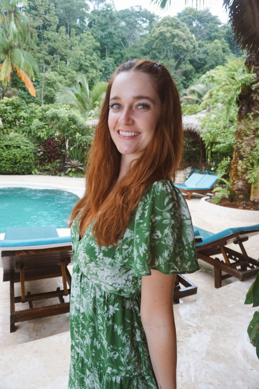 A guest in a green dress smiling beside the jungle pool