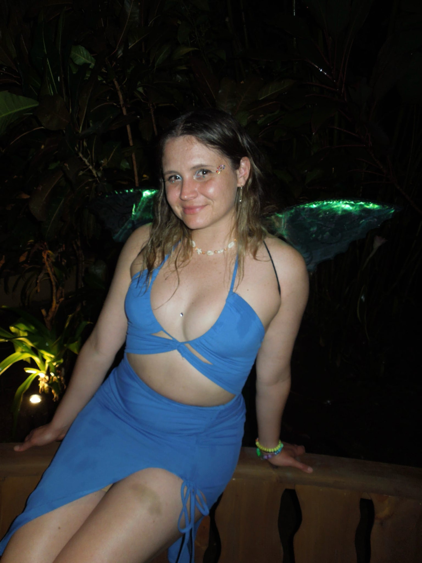 A guest in blue with glowing fairy wings in the jungle at night
