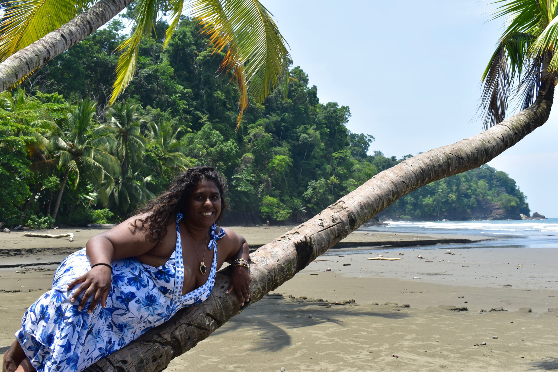 Guest smiling on a leaning palm beside the beach