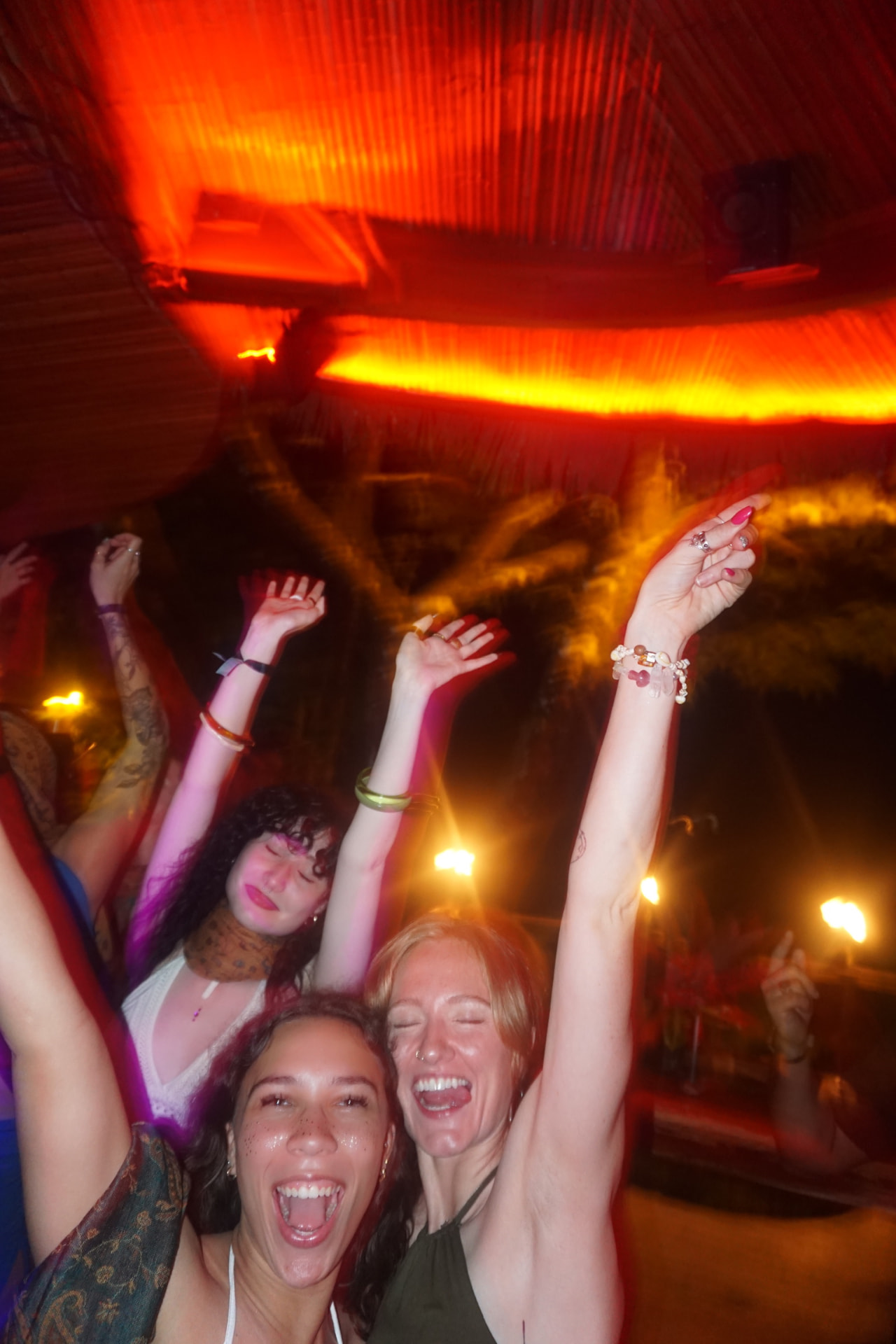 Three friends dancing with arms raised under red party lights
